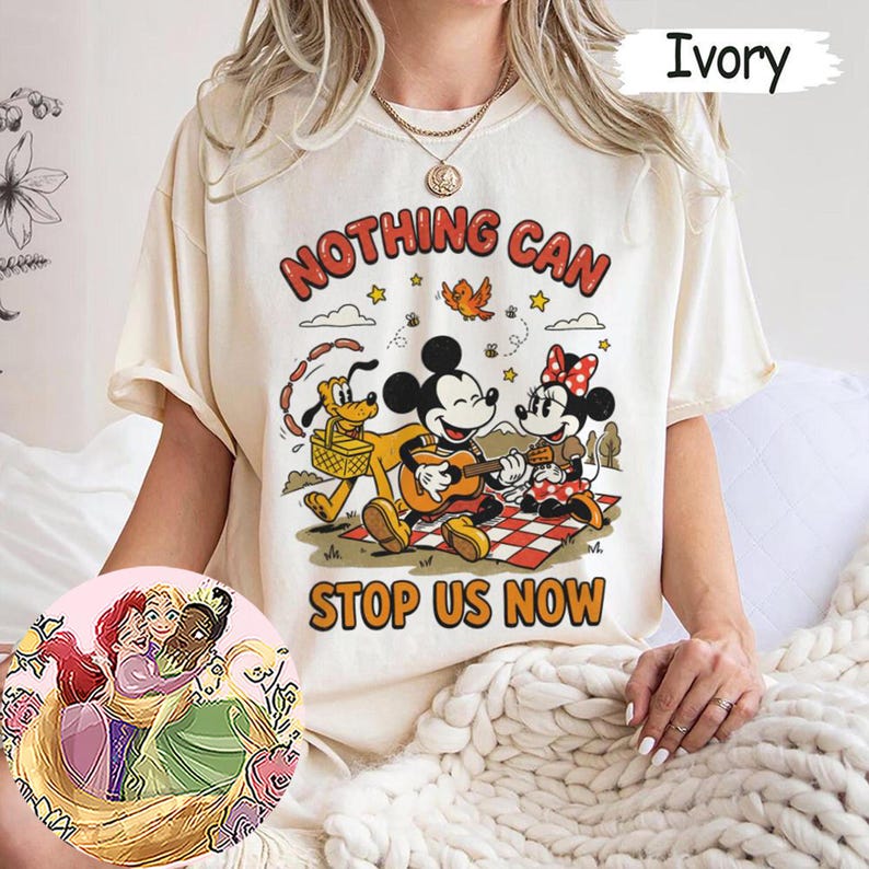May include: An ivory t-shirt featuring a graphic of Mickey Mouse playing a guitar, Minnie Mouse, and Pluto on a picnic blanket. The text reads NOTHING CAN STOP US NOW. A circular inset shows an illustration of three animated characters hugging.