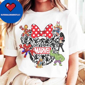 May include: White t-shirt featuring a red polka-dot bow and a heart-shaped design filled with Marvel characters. Includes Iron Man, Spider-Man, Hulk, and Minnie Mouse. The word "MARVEL" is printed in white.