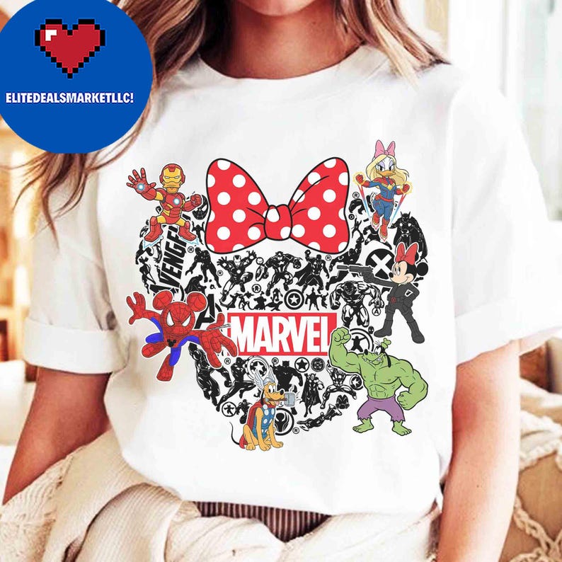 May include: White t-shirt featuring a red polka-dot bow and a heart-shaped design filled with Marvel characters. Includes Iron Man, Spider-Man, Hulk, and Minnie Mouse. The word "MARVEL" is printed in white.