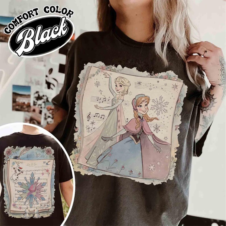 Pu&ograve; includere: T-shirt nera Comfort Color con una grafica di due principesse animate, note musicali e dettagli floreali. Un'immagine pi&ugrave; piccola &egrave; in basso a sinistra. La parola "Black" &egrave; in un ovale bianco in alto a sinistra.