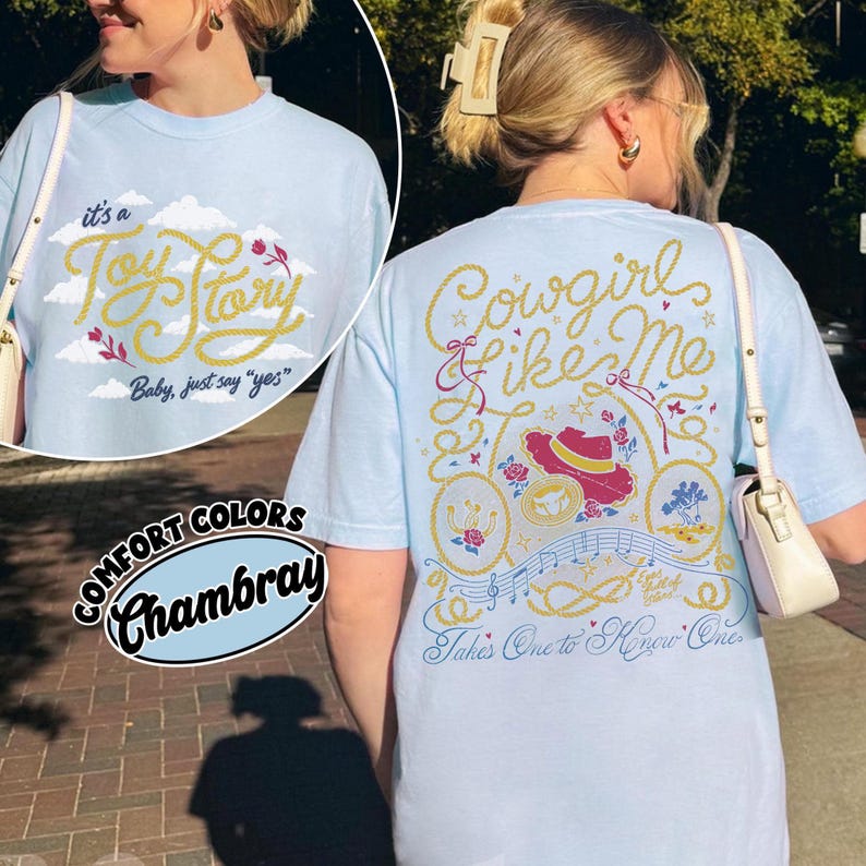 May include: A light blue t-shirt featuring a graphic print on the back with the text Cowgirl like Me and Takes One to Know One, alongside illustrations of a hat, musical notes, and rope. The front shows the text it's a Toy Story Baby, just say yes.