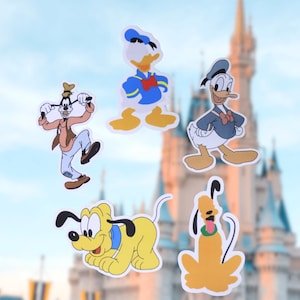 May include: Five colorful Disney character stickers: Goofy, Donald Duck, and Pluto. Goofy is in a brown outfit, Donald Duck in a blue sailor suit, and Pluto in yellow. The background features a castle under a blue sky.