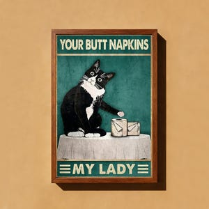 May include: A framed wall art print featuring a black and white tuxedo cat sitting on a table with two rolls of toilet paper. The text at the top reads YOUR BUTT NAPKINS and the text at the bottom reads MY LADY, set against a dark teal background.
