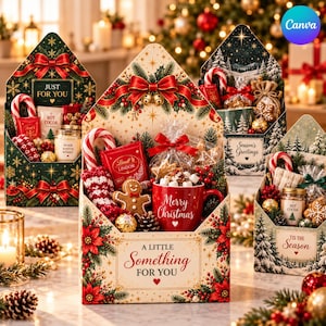 Può includere: Quattro scatole regalo decorative a forma di busta con temi natalizi. La scatola centrale mostra il testo A LITTLE SOMETHING FOR YOU e contiene una tazza rossa con la scritta Merry Christmas, un biscotto di pan di zenzero e cioccolatini.