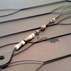 May include: Four black threaders with loops at the ends. One threader has a string of brown, white, and beige beads.