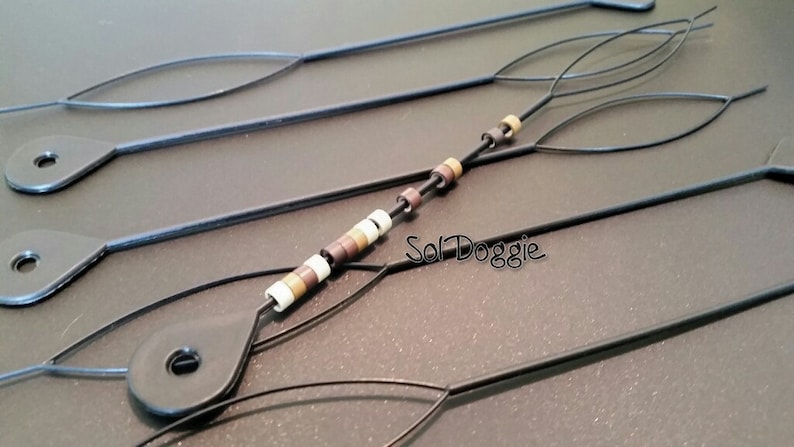 May include: Four black threaders with loops at the ends. One threader has a string of brown, white, and beige beads.