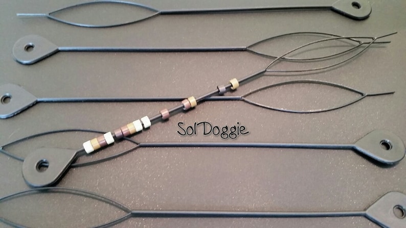 May include: Five black beading tools with a loop at one end and a pointed end. One tool has a string of brown, white, and gold beads threaded through it. The text "Sol Doggie" is visible on the surface.