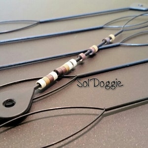 May include: Five black plastic crochet hooks with a beaded loop on one hook. The beads are brown, white, and beige. The text "Sol Doggie" is visible in the image.