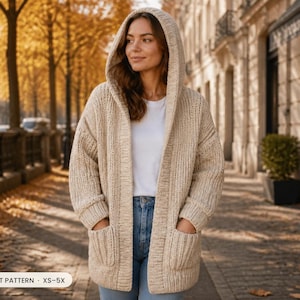 Op de afbeelding: Een beige vest met capuchon, een grove breistructuur, lange mouwen en twee opgestikte zakken aan de voorzijde. Het kledingstuk wordt gedragen over een wit t-shirt en een blauwe spijkerbroek. Een label linksonder toont de tekst CROCHET PATTERN XS-5X.