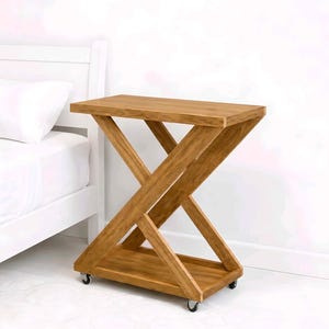 May include: A wooden side table with a unique X-shaped base and a rectangular top. The table is made of light brown wood and has a lower shelf. It sits on small caster wheels for easy movement. The table is approximately 24 inches tall.