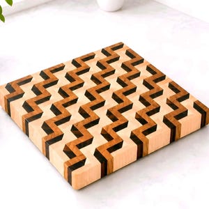 May include: A wooden cutting board with a geometric zigzag pattern. The board features alternating light and dark wood tones, creating a visually striking design. The board is square-shaped and suitable for kitchen use.