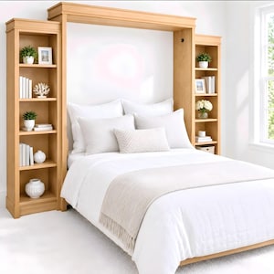 May include: A light wood wall bed unit featuring two tall, integrated side bookcases with open shelving. The bed is dressed in white bedding, including a textured throw blanket and several pillows, creating a cohesive furniture arrangement.