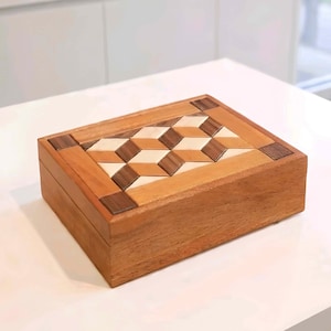 May include: A handcrafted wooden box with a geometric design on the lid. The box is made of various wood tones, including light and dark brown, and beige. The lid features a repeating pattern of angled shapes. The box is rectangular and appears to be well-made.