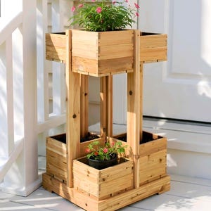 Könnte beinhalten: Ein mehrstöckiger Holzpflanzer mit drei quadratischen Boxen für Pflanzen. Der Pflanzer ist aus hellfarbenem Holz gefertigt und hat eine natürliche Oberfläche. Die obere Box enthält eine Pflanze mit rosa Blüten, und die untere Box enthält eine Pflanze mit roten Blüten.