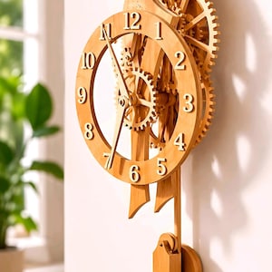 May include: A wooden wall clock with visible gears and a pendulum. The clock face features large, stylized numerals. The clock is made of light-colored wood and is mounted on a white wall. The clock's design emphasizes the mechanical workings.
