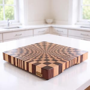 May include: A wooden cutting board with a unique optical illusion design. The board features a checkerboard pattern that appears to warp towards the center. The edges are made of alternating light and dark wood. A small metal plaque is affixed to the side.
