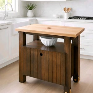 Peut inclure: Îlot de cuisine en bois avec un dessus en bloc de boucher de couleur claire et une base marron foncé. L'îlot possède une étagère inférieure et une porte d'armoire. Il comporte un trou dans le dessus et des roues pour la mobilité. Un bol blanc est sur l'étagère.
