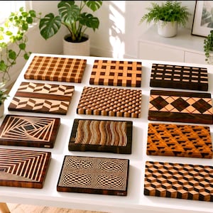 Può includere: Una collezione di dodici taglieri rettangolari in legno disposti su un tavolo bianco. Ogni tagliere presenta un distinto motivo geometrico creato da venature del legno chiare e scure a contrasto, inclusi disegni a scacchi, chevron e cubi 3D.