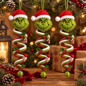 May include: Three hanging crochet ornaments featuring a green character head wearing a red and white Santa hat. Below the head is a spiral body in red, white, and green with holly leaves, red berries, and small candy canes, ending in a green bell.