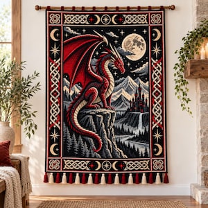 May include: A rectangular wall hanging featuring a red dragon perched on a cliffside, a full moon, and a castle. The tapestry has a black border with white Celtic knotwork, stars, and crescent moons, finished with alternating red and white tassels.