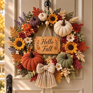 May include: A crochet autumn wreath featuring orange, green, white, and purple pumpkins, yellow sunflowers, red berries, and fall-colored leaves. A central wooden sign displays the text Hello Fall, and a beige crochet bow hangs at the bottom.