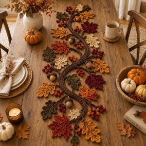 May include: A knitted table runner featuring a winding vine design adorned with crocheted autumn leaves in shades of red, orange, yellow, and brown, interspersed with small clusters of berries and acorns, laid flat on a wooden dining table.