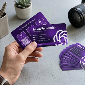 May include: A stack of rectangular business cards with a purple gradient background. The cards feature the name Johan Fernandez, the title Artificial Intelligence Manager, contact details, a QR code, and a white abstract logo on the right side.