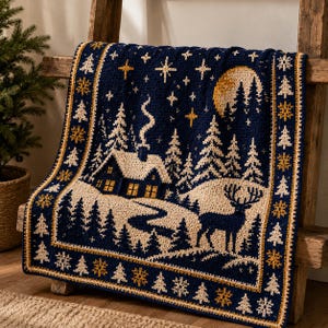 May include: A navy blue and cream crochet blanket featuring a winter landscape with a cabin, pine trees, a deer, and a moon. The border is decorated with repeating patterns of pine trees and snowflakes in gold, cream, and navy blue yarn colors.