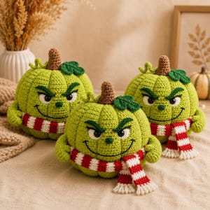 May include: Three round, lime green crocheted pumpkins featuring embroidered angry facial expressions, brown stems, and small green leaves. Each pumpkin is wrapped in a red and white striped crocheted scarf with fringed ends.