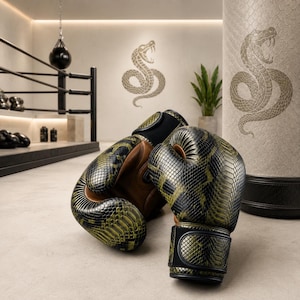 Puede incluir: Un par de guantes de boxeo con un patrón texturizado de piel de serpiente en verde y negro, forro interior marrón y correas negras para las muñecas. Los guantes están colocados frente a un saco de boxeo que muestra un gráfico de serpiente.