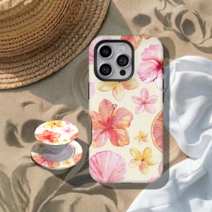 Può includere: Una custodia e un supporto per telefono con un motivo floreale di fiori di ibisco, conchiglie e una fetta di pompelmo. La custodia e l'impugnatura hanno uno sfondo color crema con accenti rosa, arancioni e gialli. Un cappello di paglia e un panno bianco sullo sfondo.