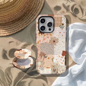 Puede incluir: Una funda de teléfono y un soporte a juego con un diseño de patchwork, que incorpora patrones florales y geométricos en tonos beige, marrón y rosa. Un sombrero de paja y tela blanca en el fondo sugieren un tema de playa.