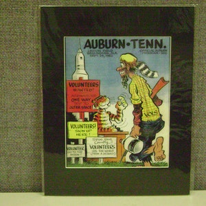 May include: A framed vintage cartoon print with the text "Auburn-Tenn." and "Volunteers Wanted!" featuring a rocket, a tiger, and a man in a yellow shirt. The print is on a black mat.