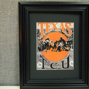 May include: A black framed print of a vintage football game poster. The poster features a large orange circle with the text "TEXAS TCU 25c" in black and white.