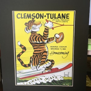 May include: A vintage program for a Clemson University football game against Tulane University. The program features a cartoon tiger on water skis with the text "Clemson Tulane", "Official Program", "Fifty Cents", "Memorial Stadium", "November 4, 1961", "Homecoming", and "Green Wave".
