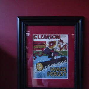 May include: A black framed picture with a vintage comic book cover featuring a cartoon tiger in a football uniform. The comic book cover reads "Clemson" and "Wake Forest".