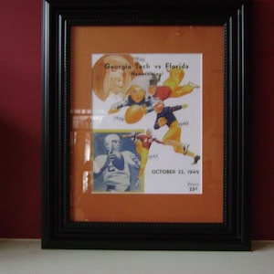May include: A framed vintage print of a college football game between Georgia Tech and Florida. The print features a collage of players from different years, with the text "Georgia Tech vs Florida Homecoming" and "October 22, 1949".