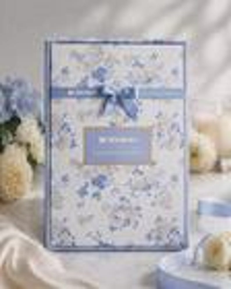 May include: A rectangular gift box with a floral pattern in shades of blue and white. The box is tied with a blue ribbon and bow. The text "Be Wonderful" is visible on a label. The background includes flowers and decorative elements.