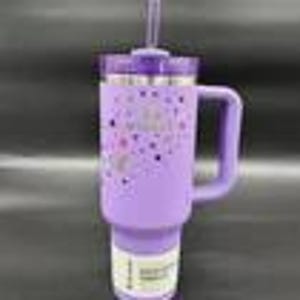 Puede incluir: Un vaso t&eacute;rmico lavanda con asa y pajita. El vaso tiene una tapa morada y un patr&oacute;n decorativo de corazones y estrellas. El vaso est&aacute; dise&ntilde;ado para contener aproximadamente 887 ml.