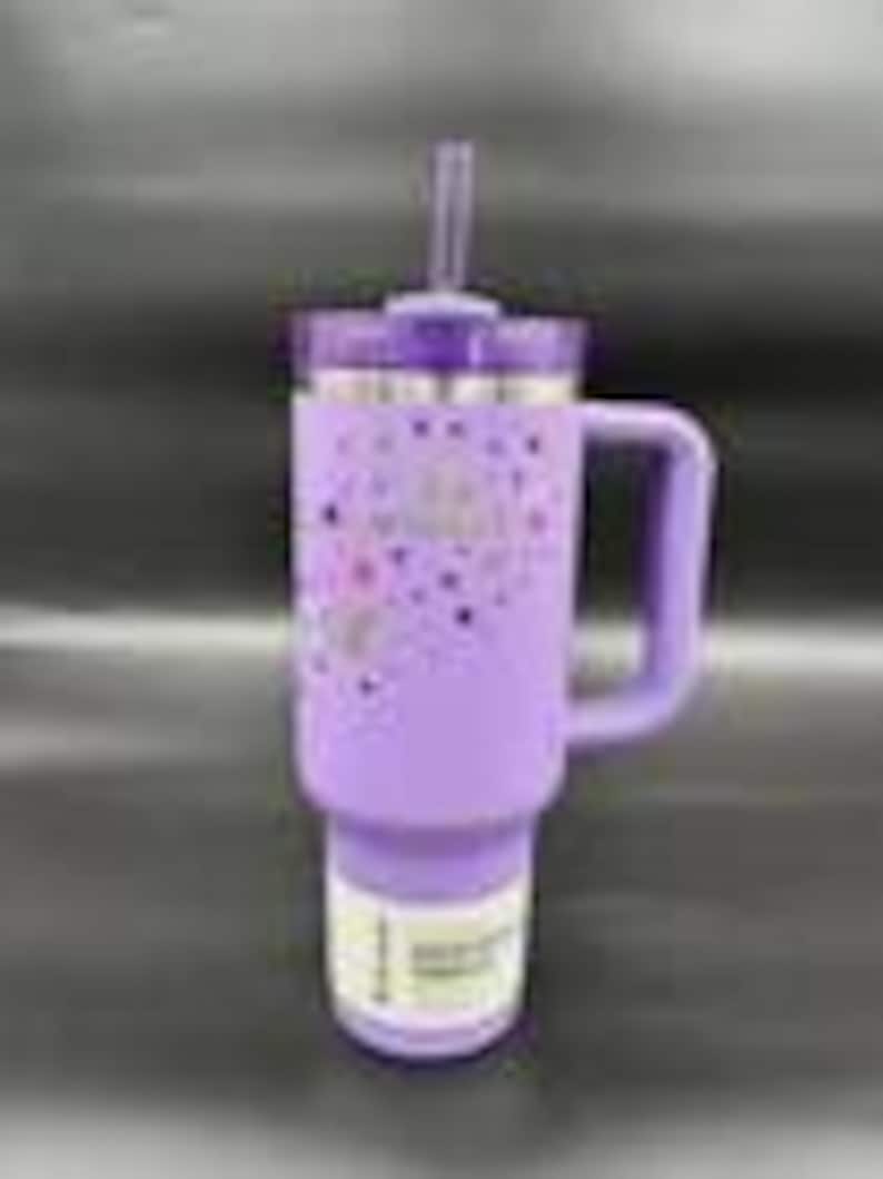 Puede incluir: Un vaso t&eacute;rmico lavanda con asa y pajita. El vaso tiene una tapa morada y un patr&oacute;n decorativo de corazones y estrellas. El vaso est&aacute; dise&ntilde;ado para contener aproximadamente 887 ml.