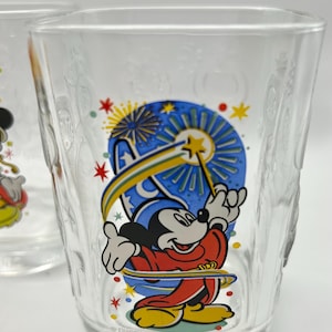 May include: Clear glass tumbler featuring a colorful graphic of Mickey Mouse in a sorcerer's outfit, holding a magic wand. The design includes stars and fireworks. The word "Disney" is printed on the glass.