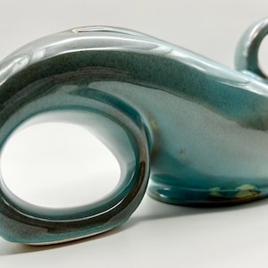 May include: A pair of teal ceramic vases with a glossy finish. One vase has a large loop, the other has a smaller loop and a handle. The vases have a unique, organic shape and are suitable for home decor.