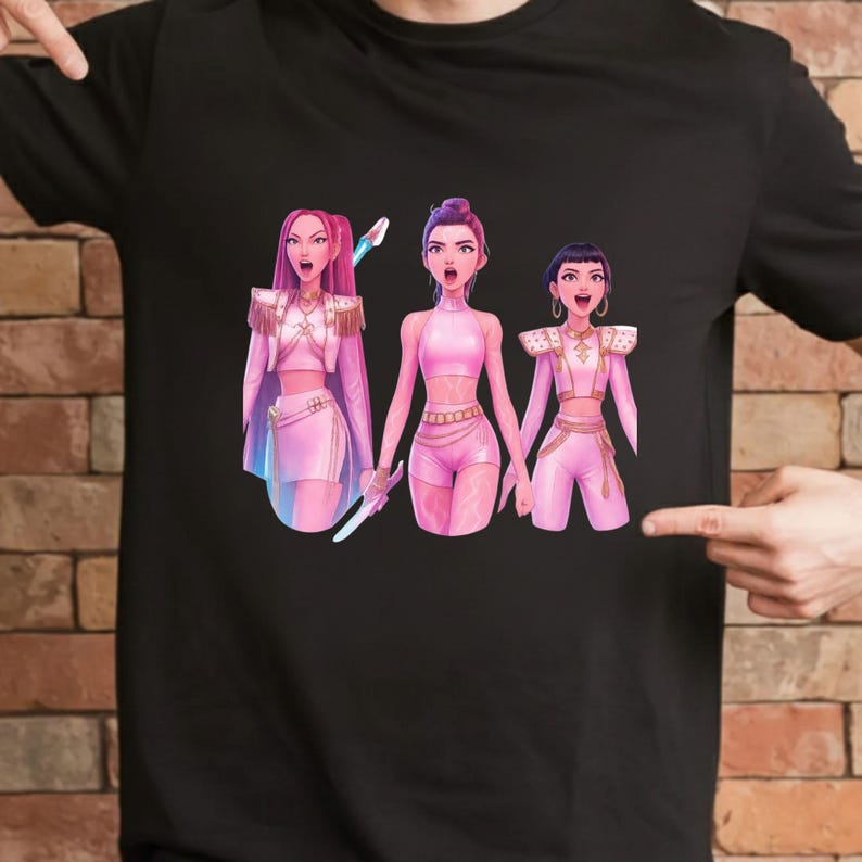 Pode incluir: Camiseta preta com um gr&aacute;fico de tr&ecirc;s figuras estilizadas em trajes rosa. As figuras t&ecirc;m a boca aberta e seguram objetos. A obra de arte tem um estilo vibrante e de desenho animado, com detalhes em rosa e branco.