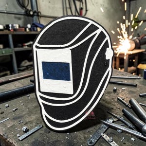 Puede incluir: Un recorte en blanco y negro de una careta de soldar con una lente rectangular azul. El diseño está delineado en blanco sobre una superficie negra texturizada, mostrando una representación estilizada del equipo de protección.