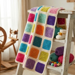 May include: A vibrant, hand-crocheted blanket with a patchwork design. The blanket showcases squares in a variety of colours, such as pink, orange, teal, purple, and yellow, set against a cream background. It is draped over a small, white wooden ladder.