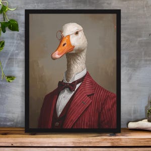 May include: Framed artwork featuring a goose wearing a red pinstripe suit, bow tie, and round glasses. The goose has a white head and orange beak. The artwork is displayed on a wooden surface.
