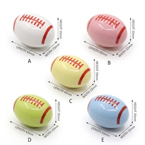 May include: Five ceramic football-shaped cabinet knobs in white, pink, yellow, light green, and light blue. Each knob features red laces and stripes, measuring 43mm in length, 33mm in width, and 30mm in height, labeled A through E respectively.