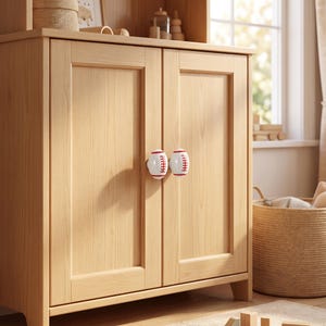 May include: A light-colored wooden cabinet featuring two doors with white and red baseball-shaped knobs. The cabinet has a smooth, natural wood grain finish and a rectangular frame design on each door, providing a clean and functional storage unit.