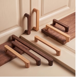 Puede incluir: Una colección de tiradores de armario rectangulares de madera en tonos claros y oscuros. Los tiradores presentan bordes redondeados y un acabado liso, dispuestos en varias posiciones sobre una superficie plana, tanto horizontal como vertical.