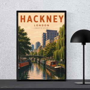 Può includere: Un poster da viaggio incorniciato raffigurante una scena di canale a Hackney, Londra, con barche sul canale, alberi ed edifici cittadini. Il testo recita HACKNEY LONDON VIBRANT BY NATURE. Una lampada da tavolo nera è posizionata a destra.